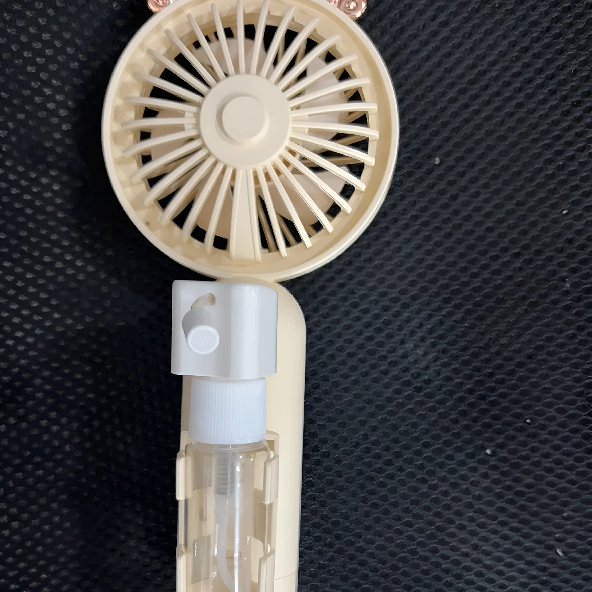 Small plastic USB desk fan with nozzle in apricot colour, shown with charging cable on a wooden desk.