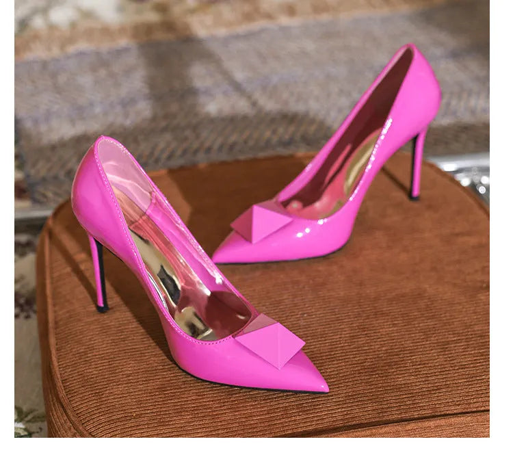 Pink patent leather women's stiletto high heels with pointed toe and decorative rivet buckle.
