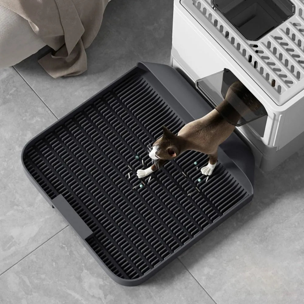 Large black cat litter pedal mat with textured grooves, placed next to a litter box.