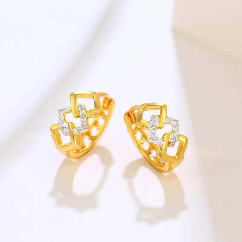 A pair of gold-coloured geometric drop earrings with a hollow out design on a plain background.