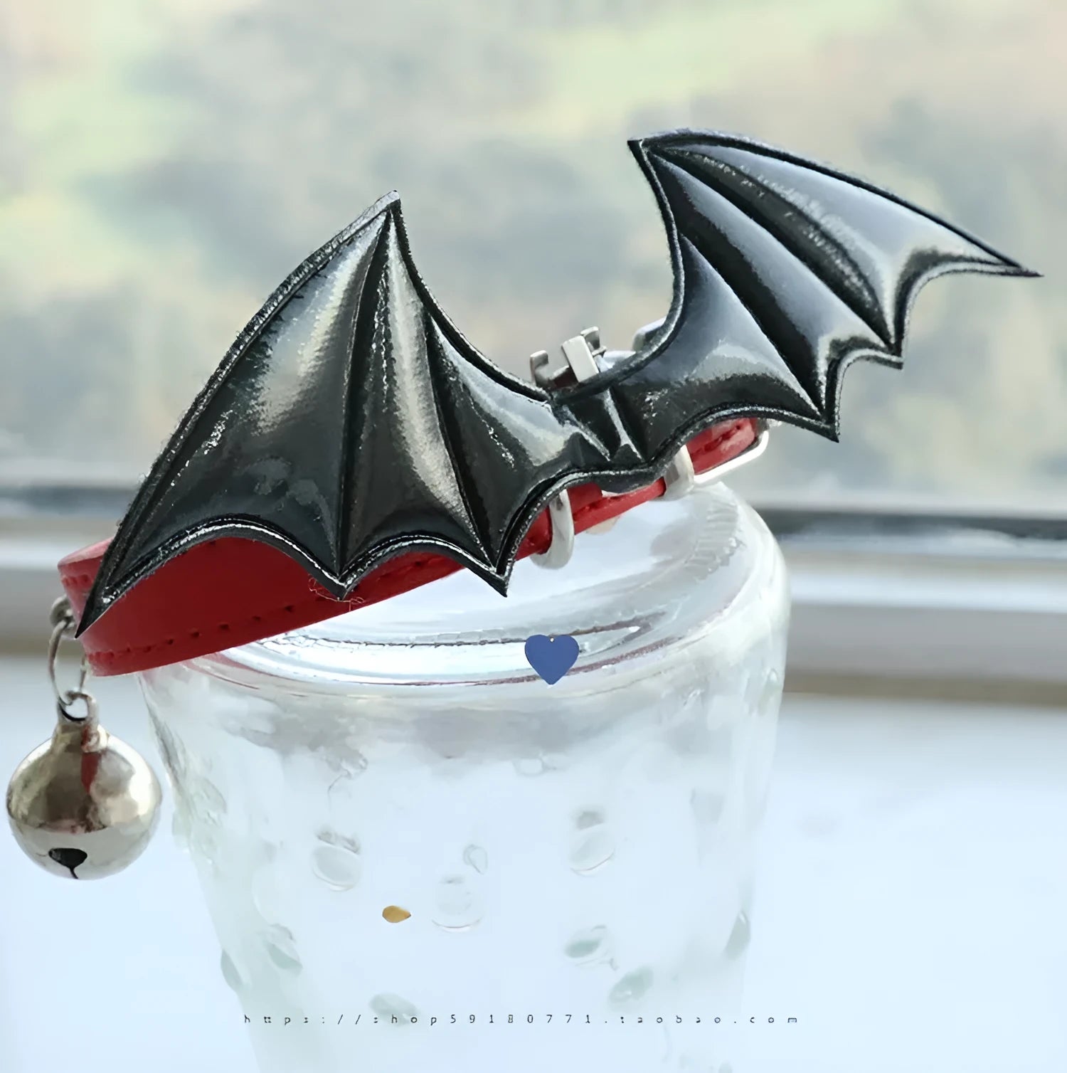 Small black patent leather pet collar with silver devil wings charm and bell on a white background.
