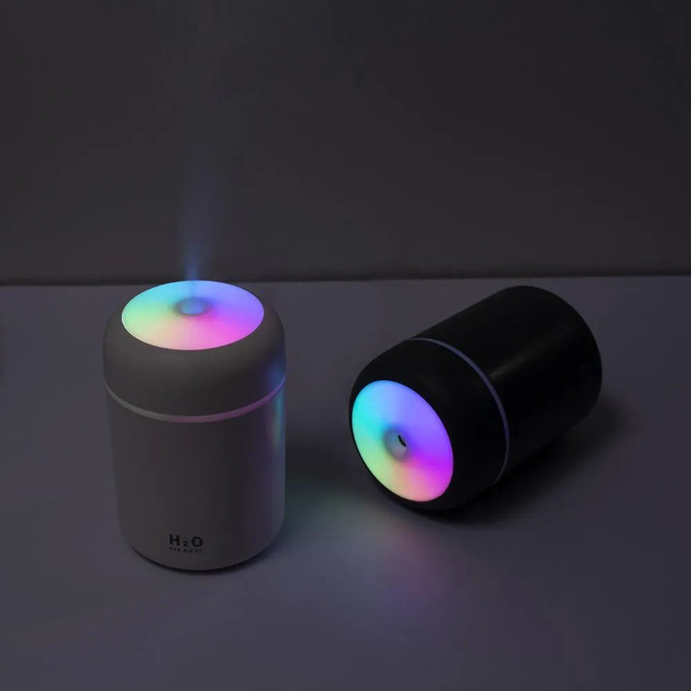 Pink USB desktop humidifier with LED lights emitting mist on a wooden desk