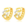 A pair of gold-coloured geometric drop earrings with a hollow out design on a plain background.