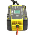 12V 24V vehicle battery charger with digital display and UK plug on a workbench.