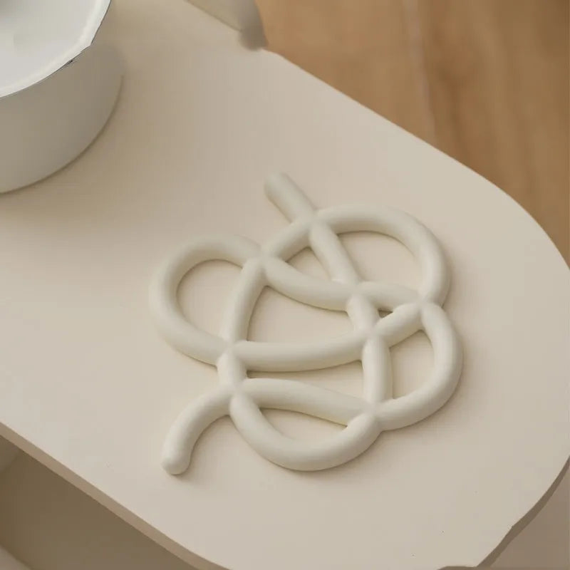 A ceramic heat-proof mat in an irregular shape on a table, shown in Bright Black, Coconut Milk Gray, and Splash Ink colour options.