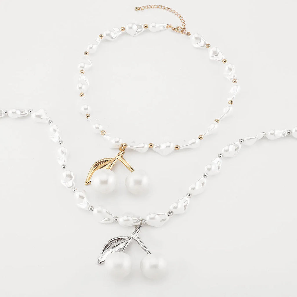 Gold geometric cherry fruit pendant on an adjustable white imitation pearl chain necklace.