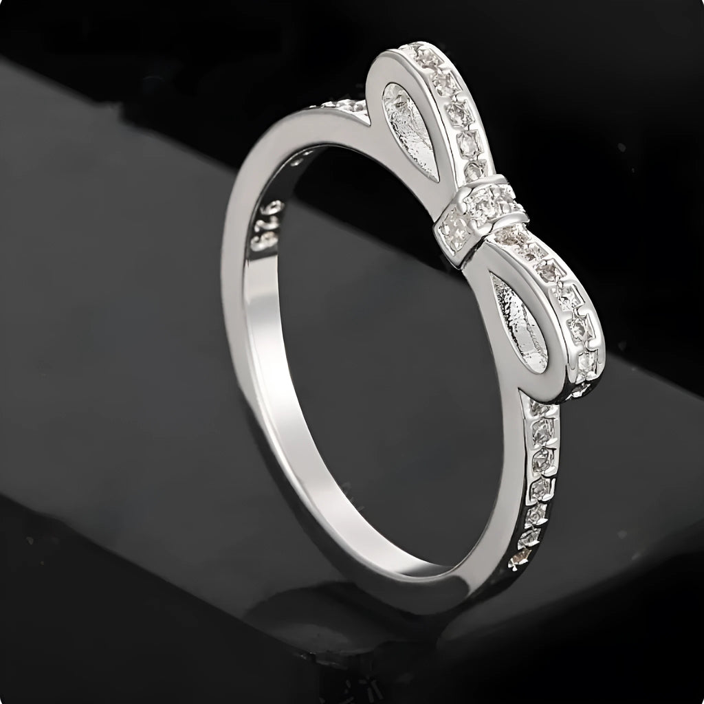 Silver coloured bow-shaped ring with sparkling rhinestone crystal details on a light background.