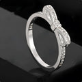 Silver coloured bow-shaped ring with sparkling rhinestone crystal details on a light background.