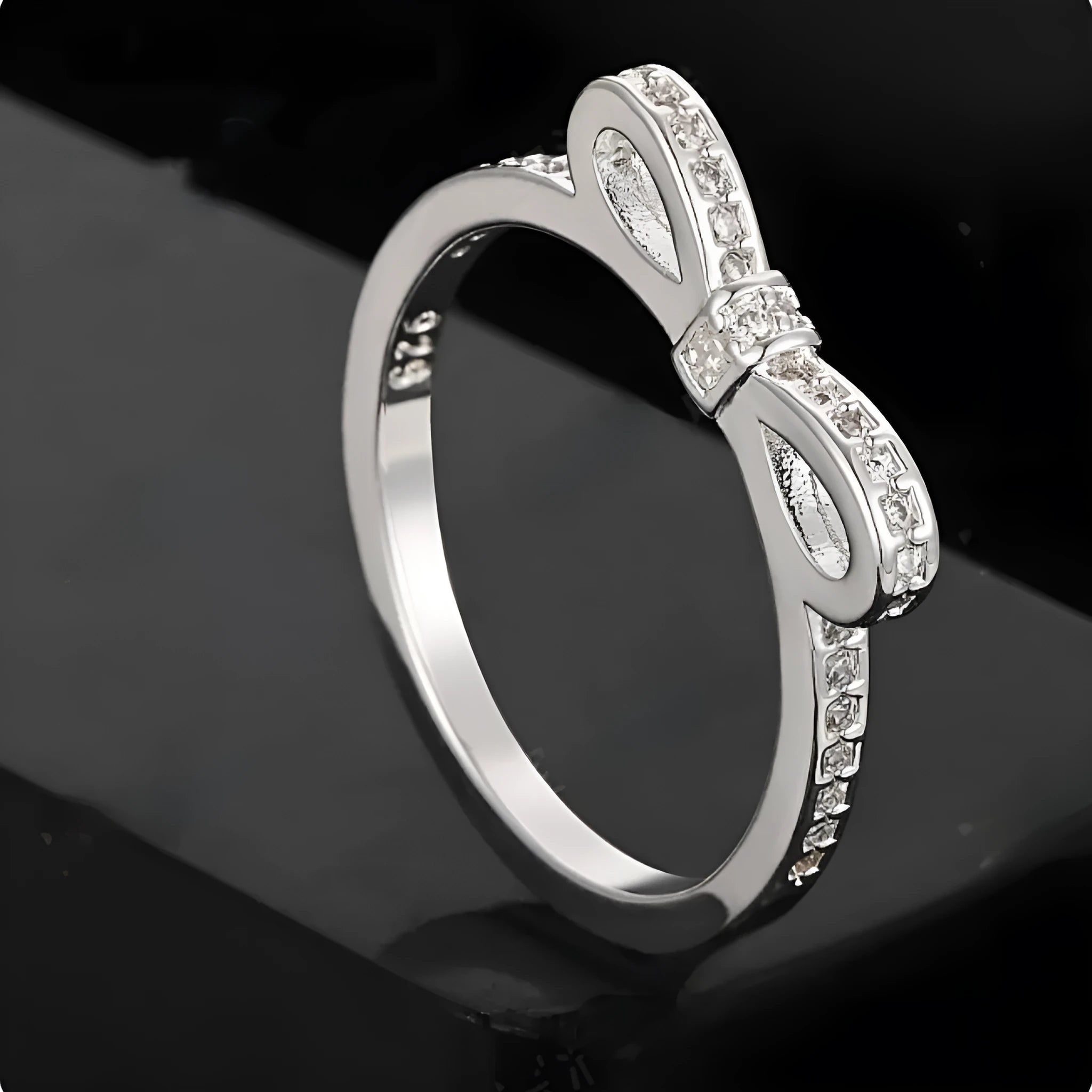 Silver bow-shaped ring set with clear rhinestone and zircon crystals on a model's hand.