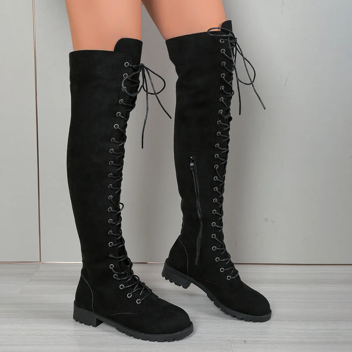 Black lace-up over-the-knee boots with round toe and flat rubber sole on a neutral background.