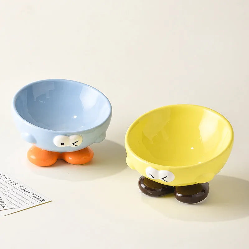 Blue and yellow ceramic slanted pet food bowls with animal face expressions for cervical spine support.