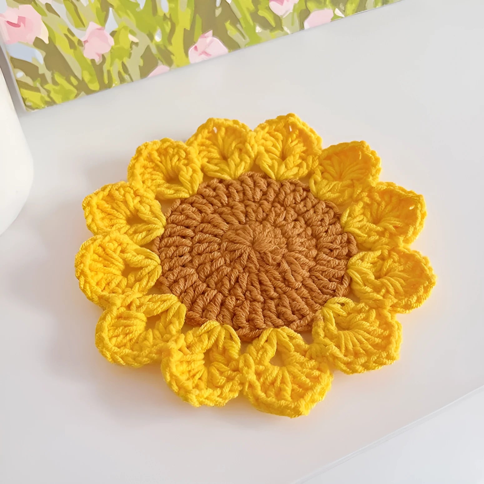 Hand-woven wool coaster with floral pattern on a wooden table.