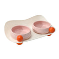 Two raised ceramic pet bowls with pink and yellow colours and grey non-slip silicone bases.