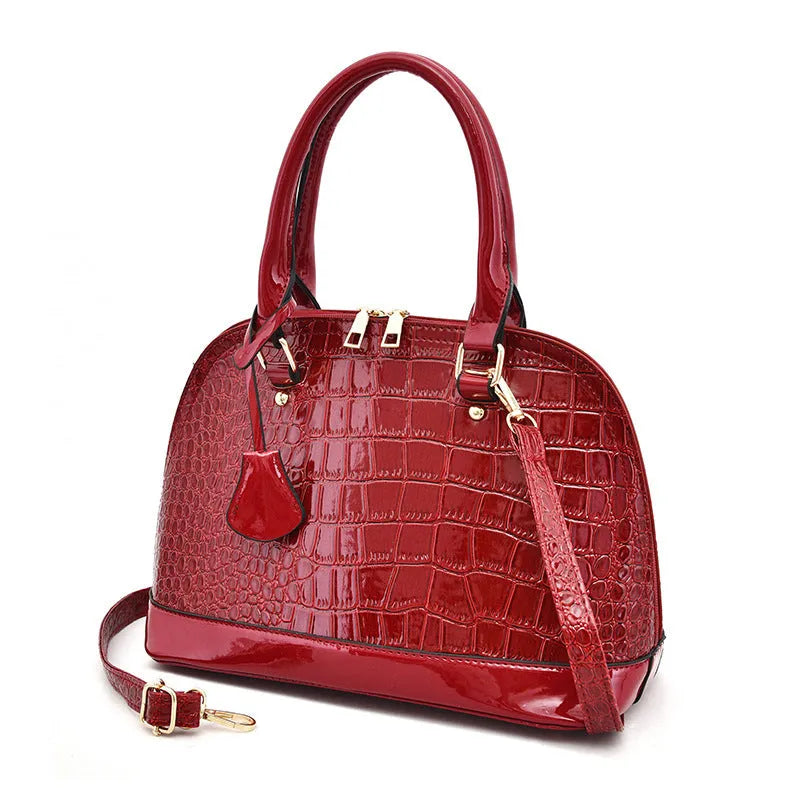 Shiny black shell-shaped crossbody bag showing front view and shoulder strap.