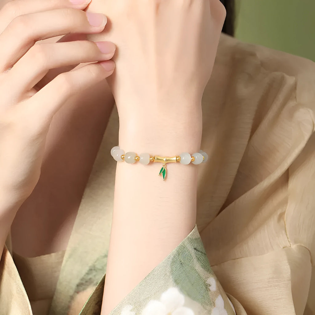 Women's bracelet with Hetian jade bead and sterling silver bamboo leaf charm on a wrist.