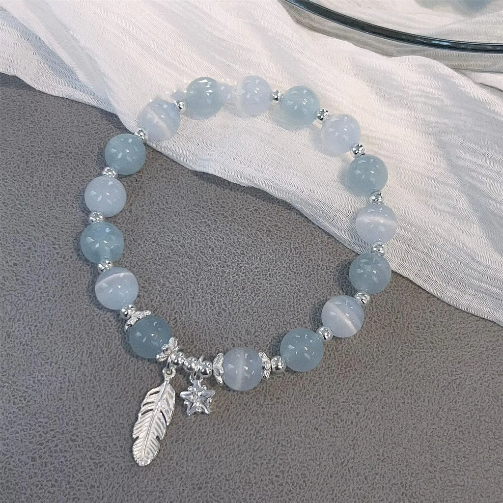 Small white crystal and glass charm bracelet with feather and blue moonlight details on wrist.