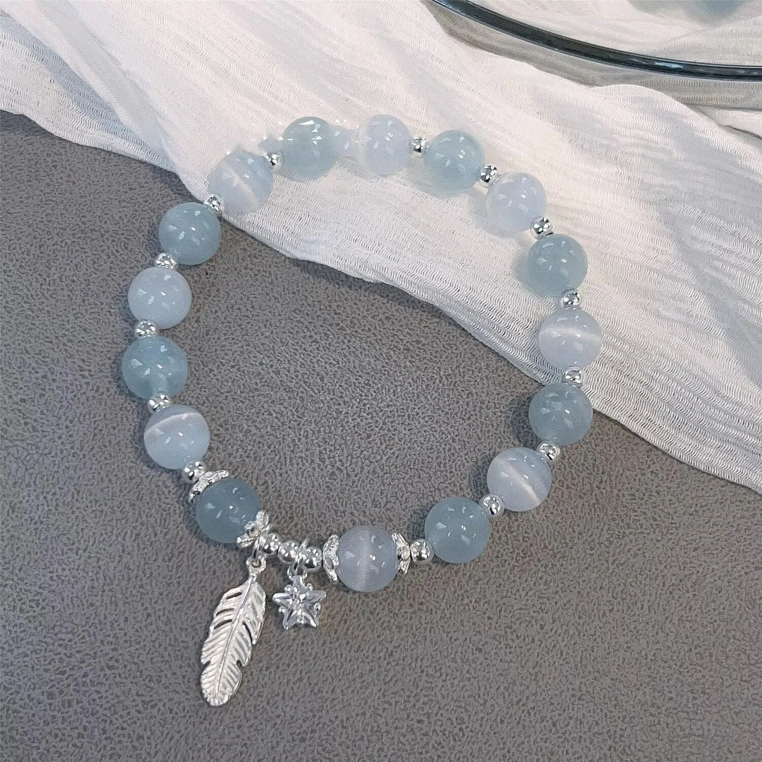 Small white crystal and glass charm bracelet with feather and blue moonlight details on wrist.
