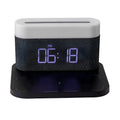 A compact black wireless charging table lamp with a digital clock display and integrated night light on a wooden desk.