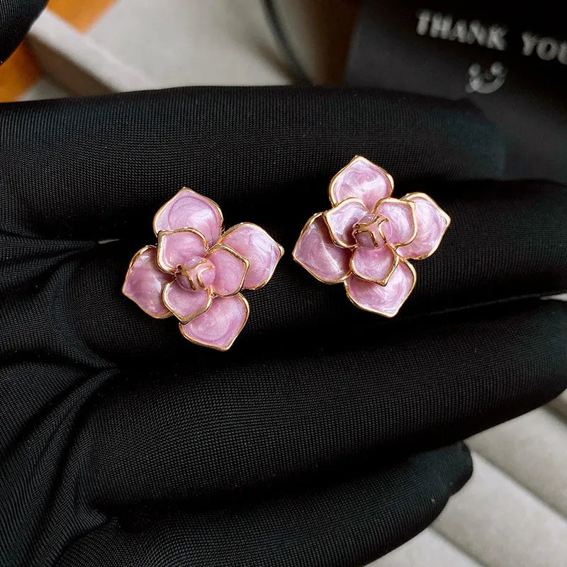 A pair of gold-plated purple flower stud earrings with an oil-spot glaze texture on a white background.