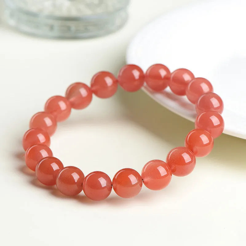Scattered polished cherry red agate beads and elastic cord for a DIY bracelet next to an assembled single-strand bracelet.