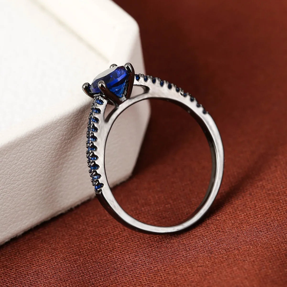 Colourful hexagon zircon copper ring in gold and gun black finishes on a size guide.