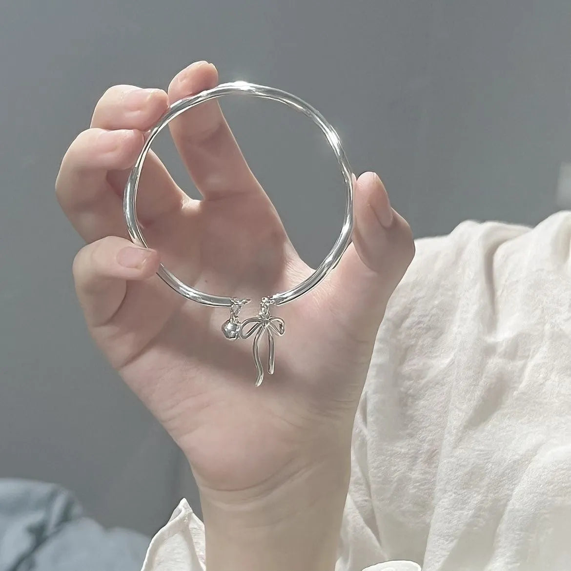 Silver coloured adjustable bracelet with a bow and bell charm on a chain.