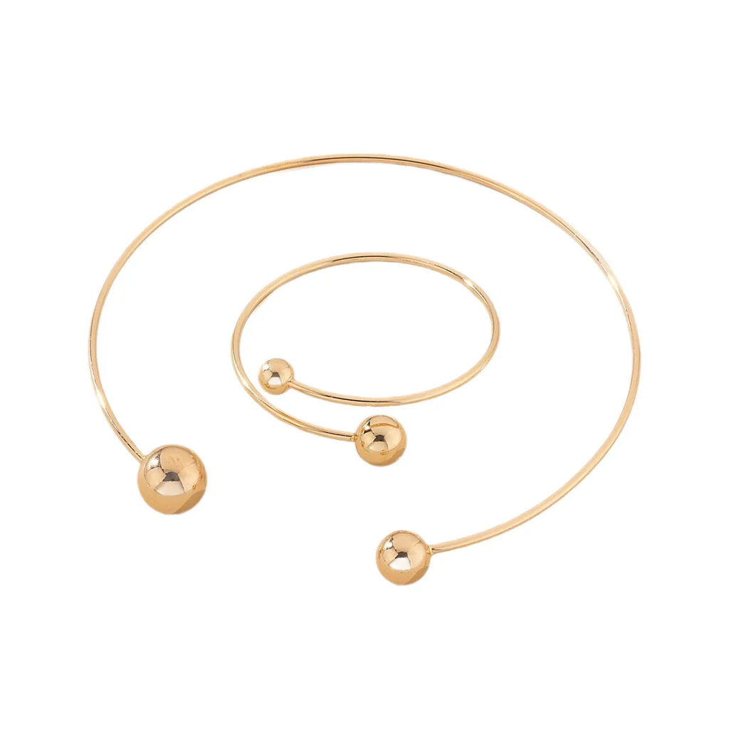 Gold dislocation ball open-end thin bangle bracelet with matching necklace on a flat surface