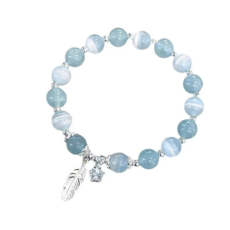 Small white crystal and glass charm bracelet with feather and blue moonlight details on wrist.