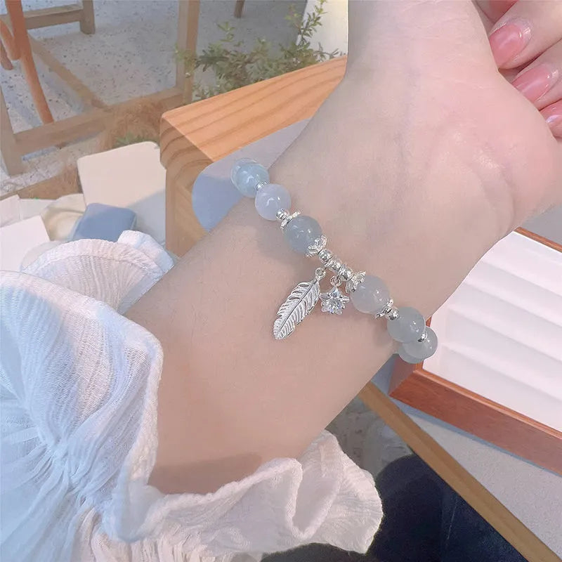 Small white crystal and glass charm bracelet with feather and blue moonlight details on wrist.