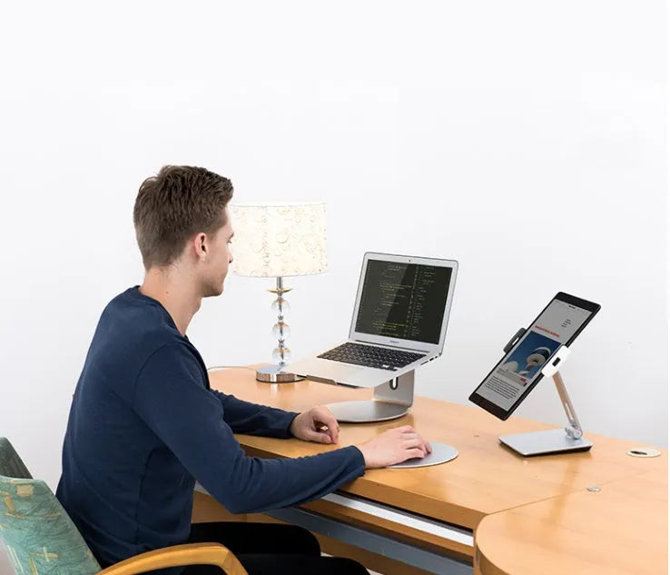 Silver foldable aluminium phone tablet stand with 360-degree rotating bracket on a desktop.