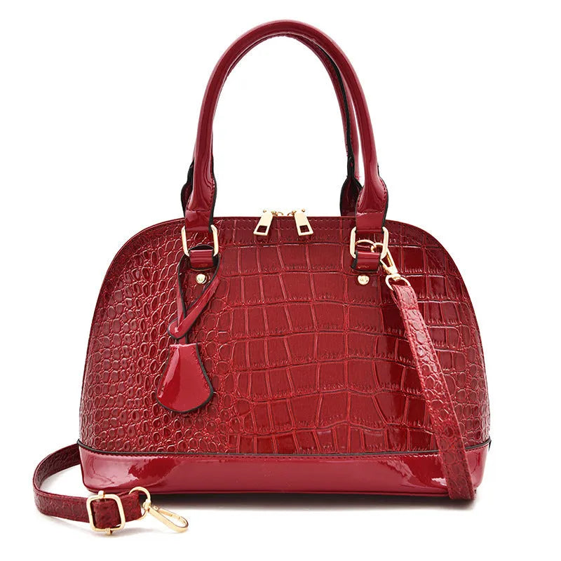 Shiny black shell-shaped crossbody bag showing front view and shoulder strap.