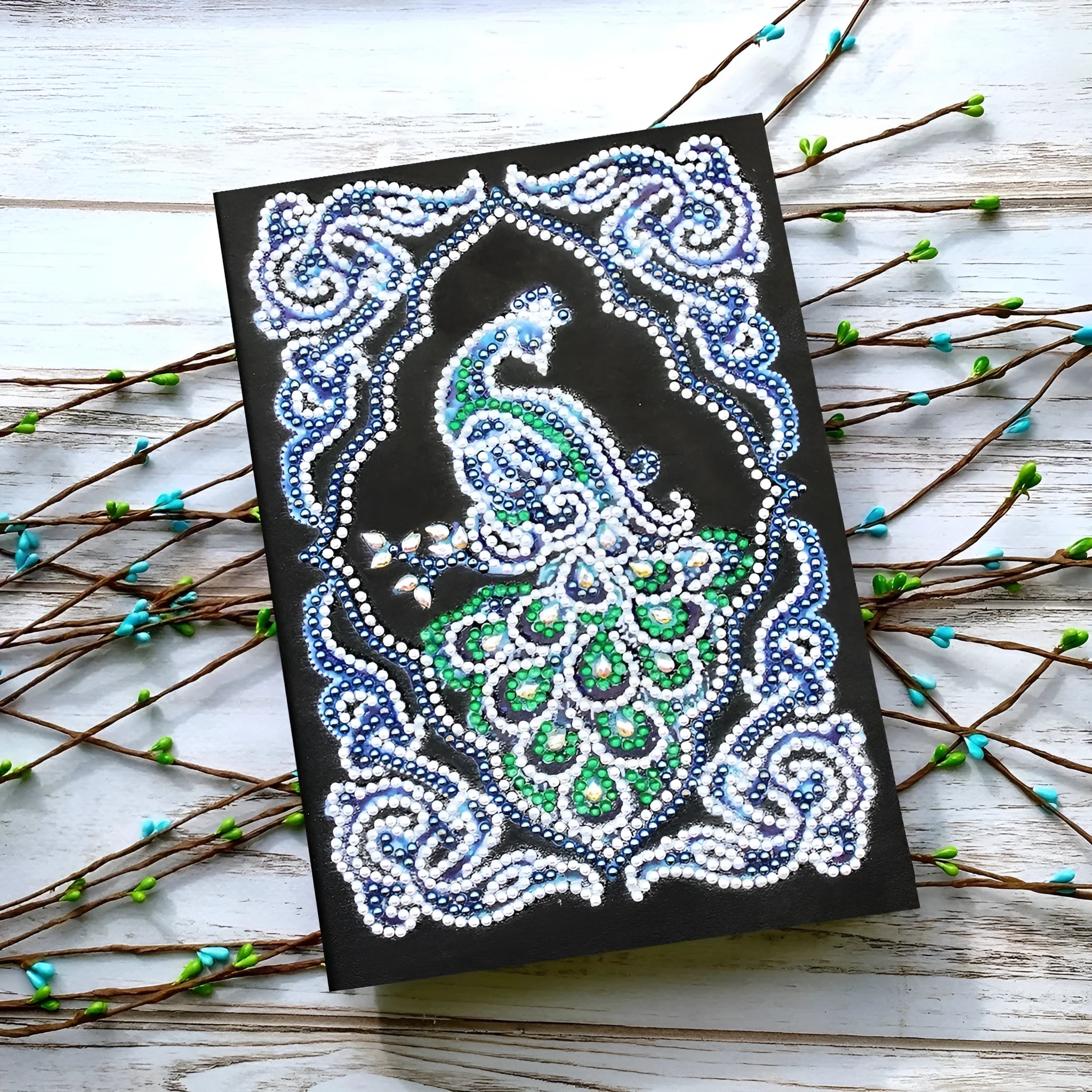 A5 black diamond painting notebook open to show peacock artwork with shaped and bright drills.