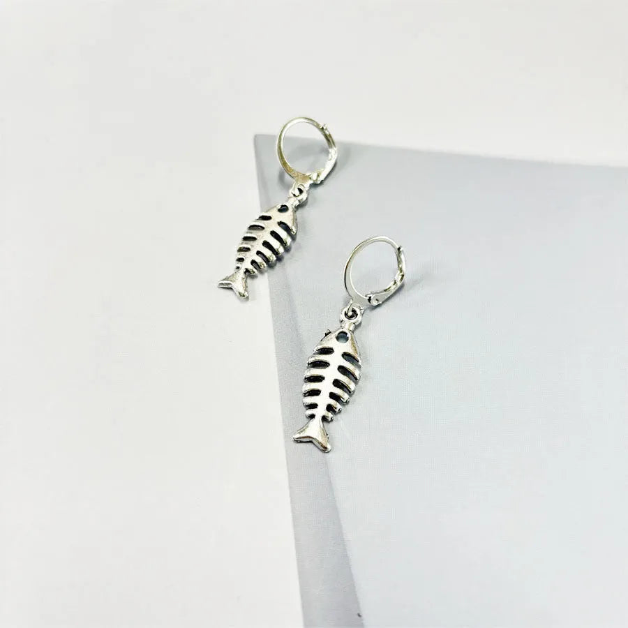 Close-up of silver fishbone pendant earrings on a white background, showing O-shaped chain detail.