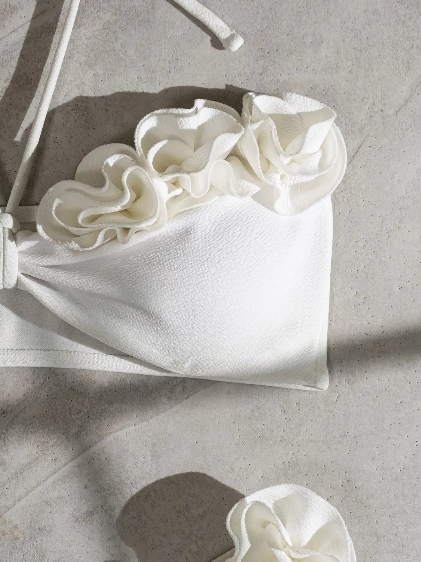 White halter bikini with lace-up front and three-dimensional floral detail on a mannequin.