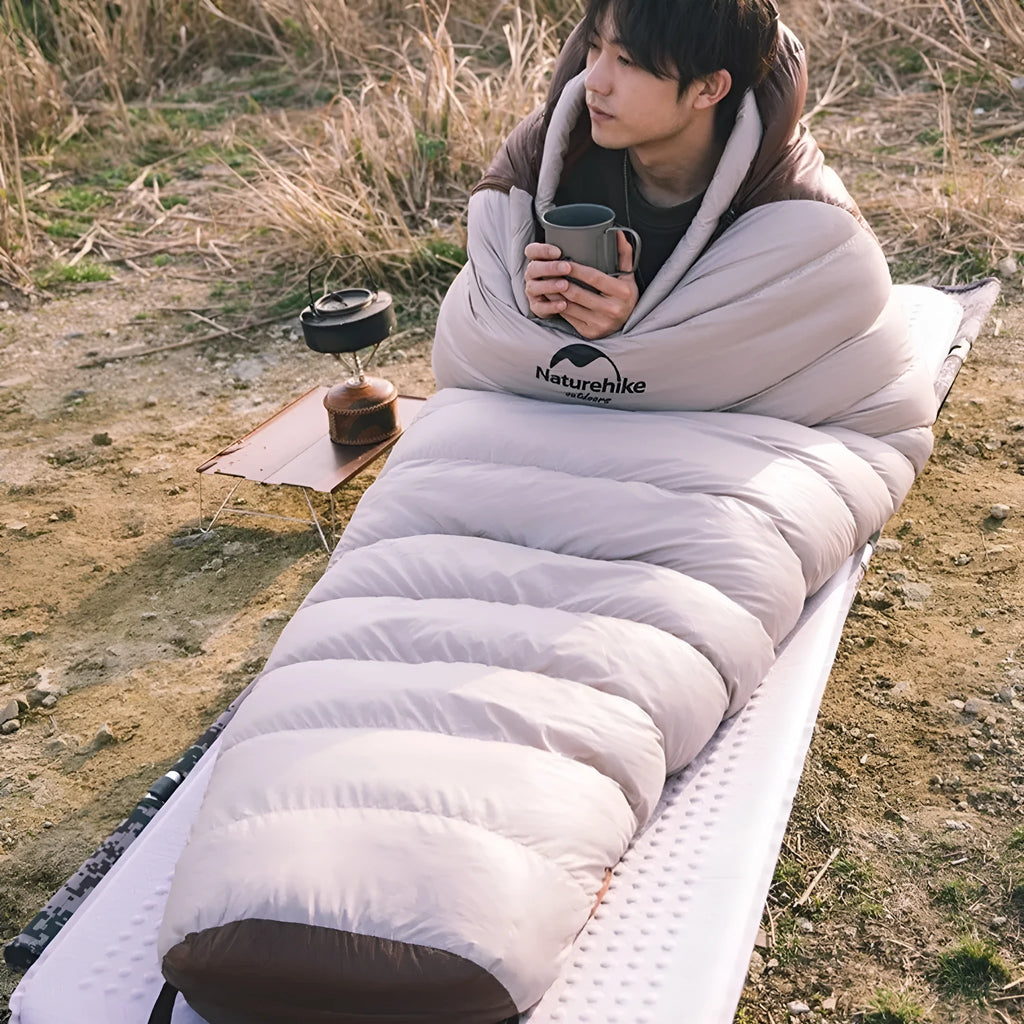 Grey mummy-style goose down sleeping bag for adults, packed in its included storage bag.