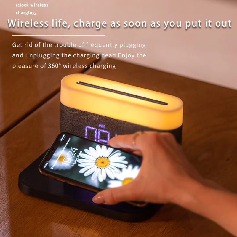 A compact black wireless charging table lamp with a digital clock display and integrated night light on a wooden desk.
