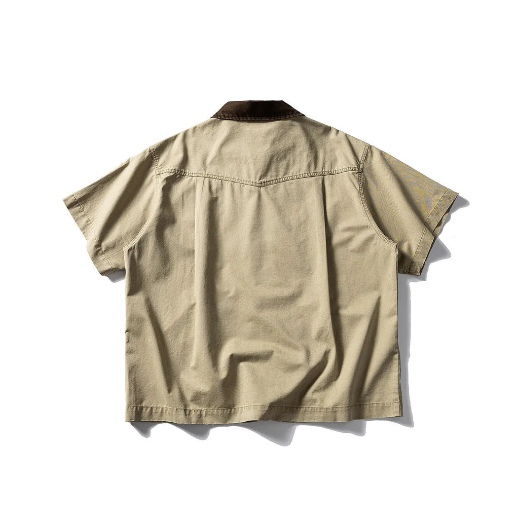 A khaki coloured, loose-fitting short sleeve cotton overalls shirt with a cardigan style on a hanger.