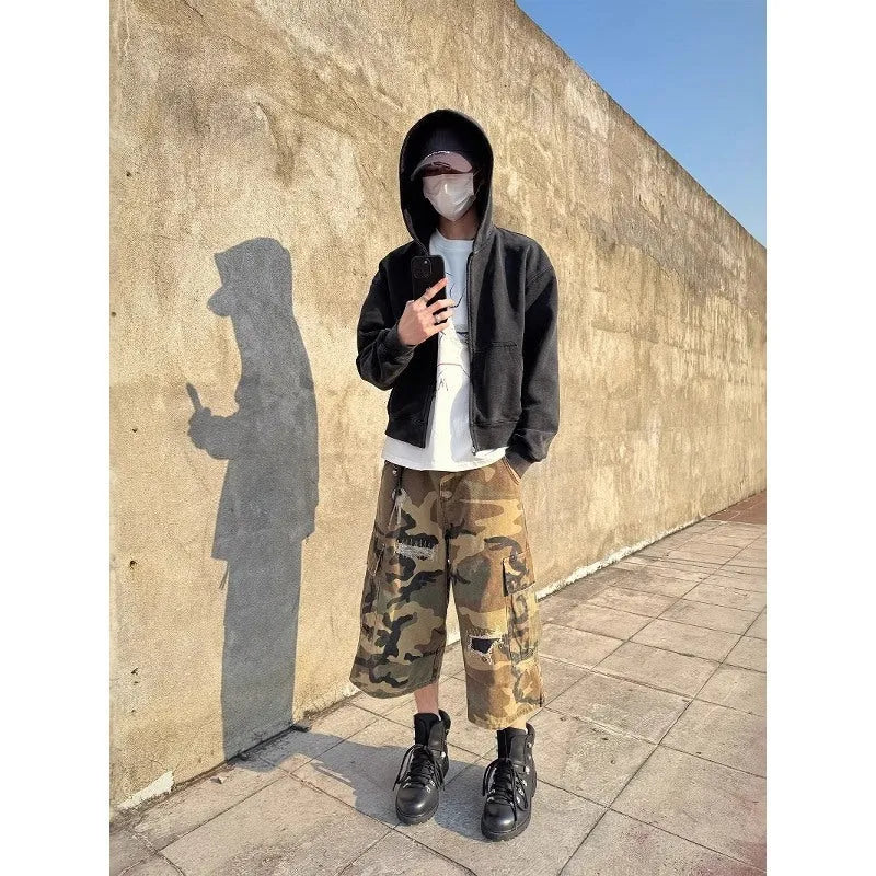 Man wearing loose straight-cut camouflage jeans with patch ripped detailing and a cropped ankle length.