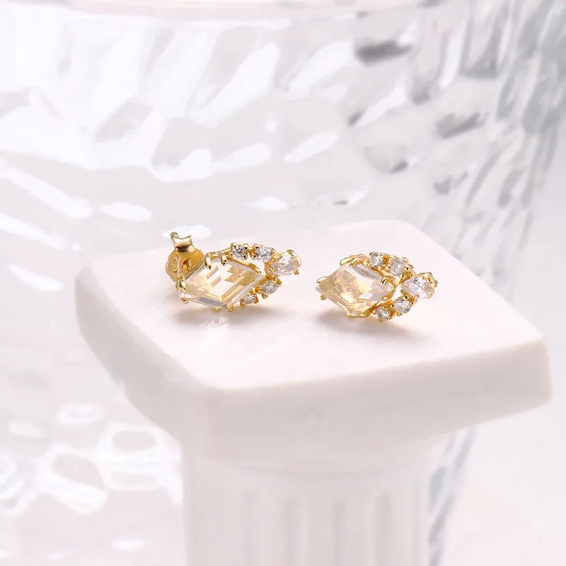 A pair of geometric shaped silver ear studs with sweet white crystal centres on a plain background.