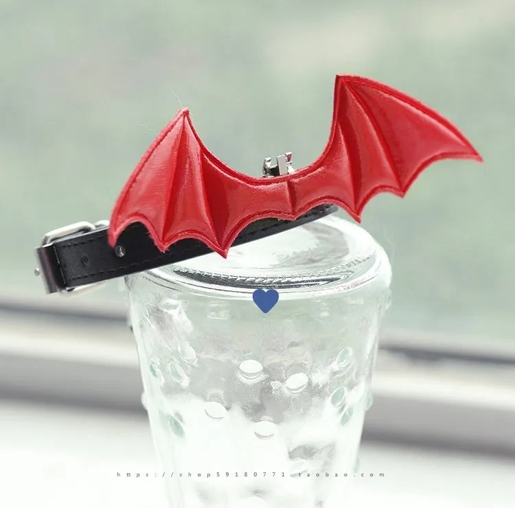 Small black patent leather pet collar with silver devil wings charm and bell on a white background.