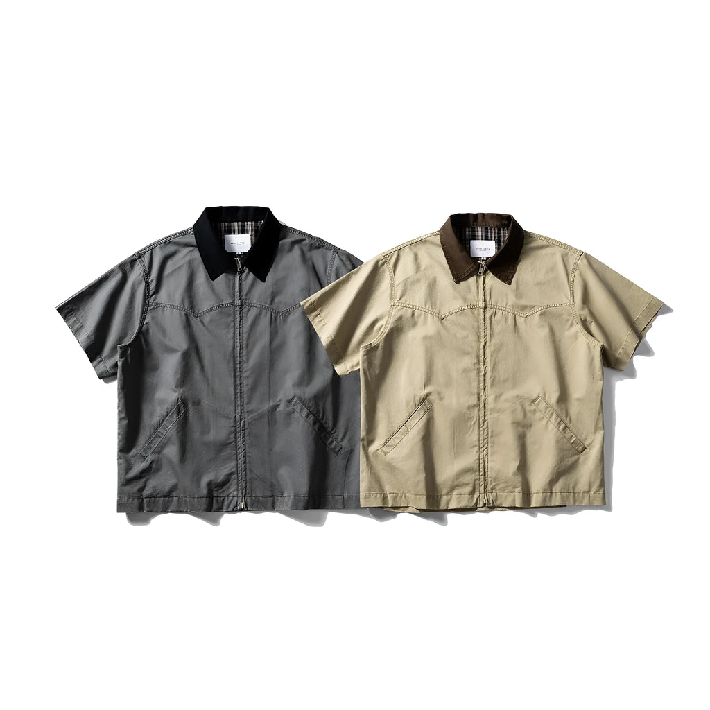 A khaki coloured, loose-fitting short sleeve cotton overalls shirt with a cardigan style on a hanger.