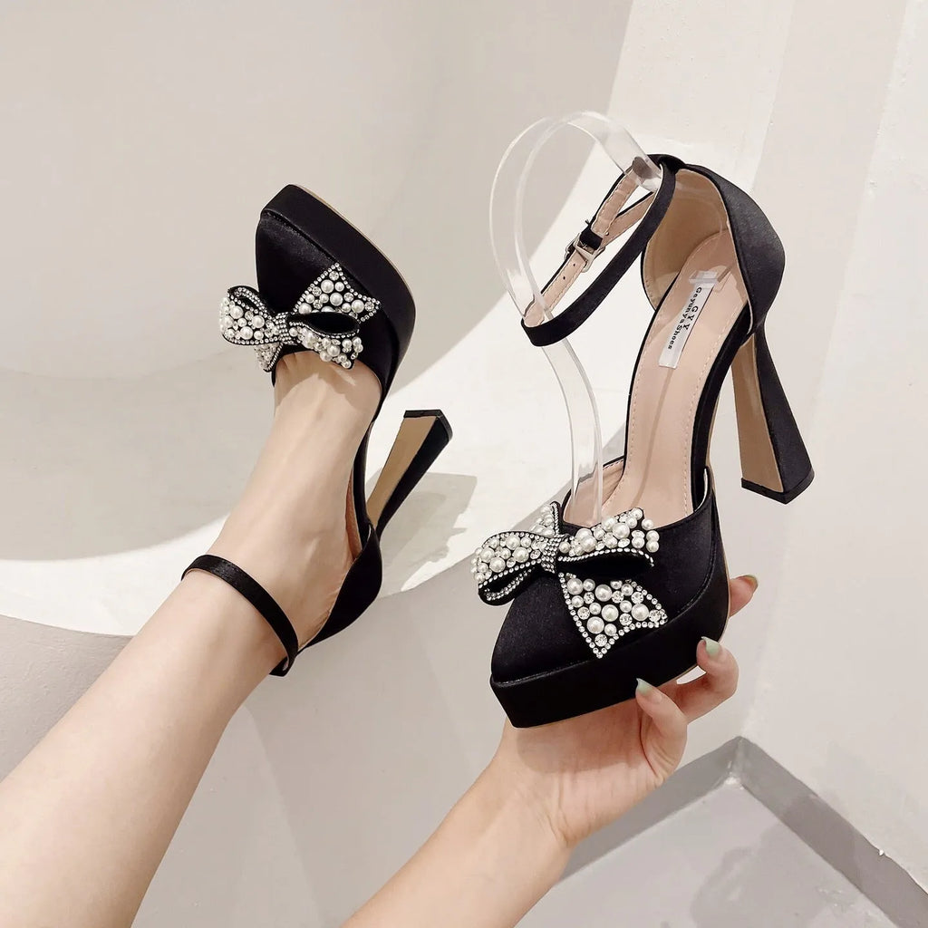 Women's black satin pointed-toe sandals with a bow detail and loop strap.