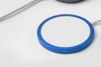 Silver MagSafe magnetic wireless charger for iPhone on a desk next to an iPhone.