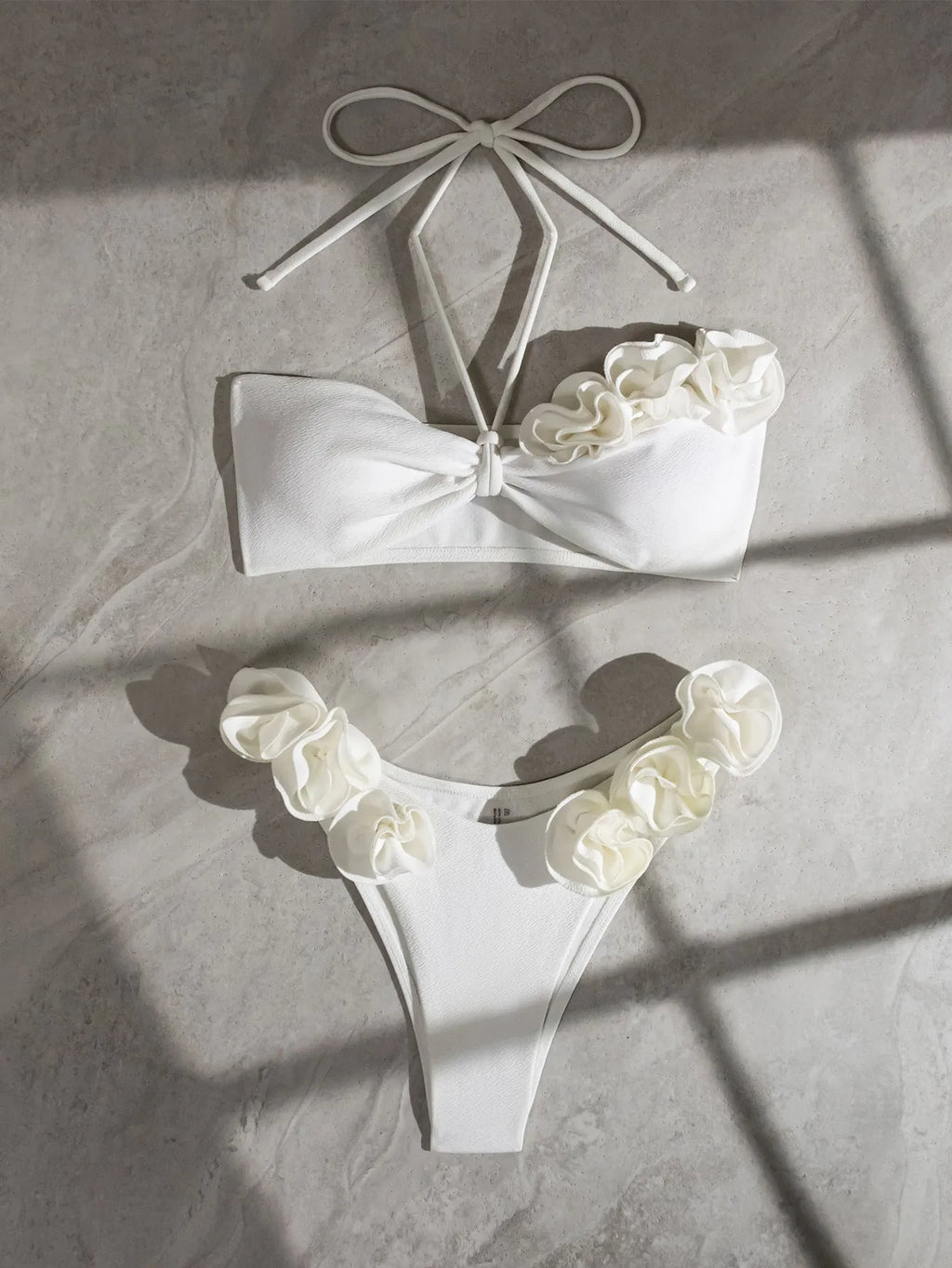White halter bikini with lace-up front and three-dimensional floral detail on a mannequin.