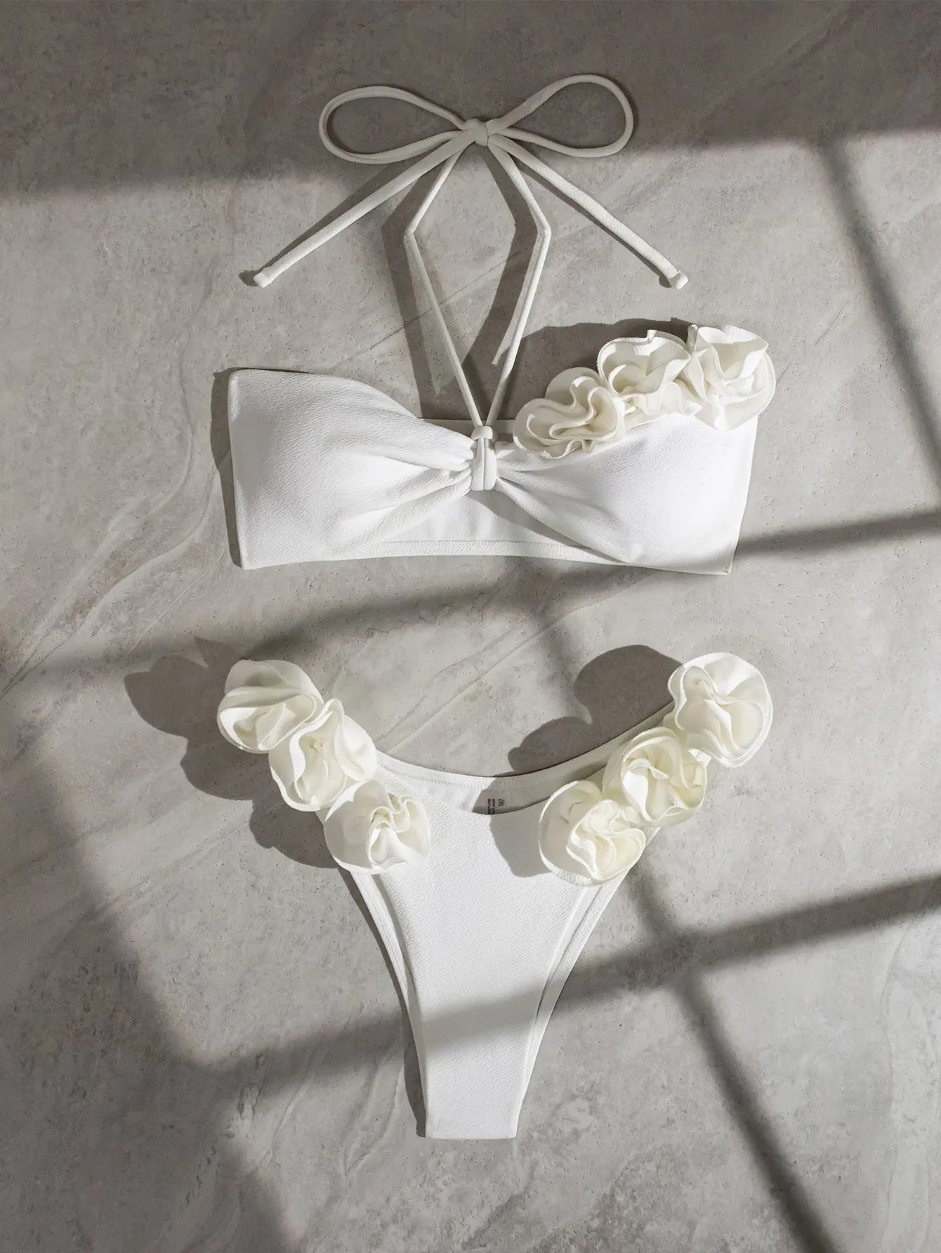 White halter bikini with lace-up front and three-dimensional floral detail on a mannequin.