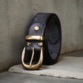 Men's black casual leather belt with copper pin buckle on a jeans background.