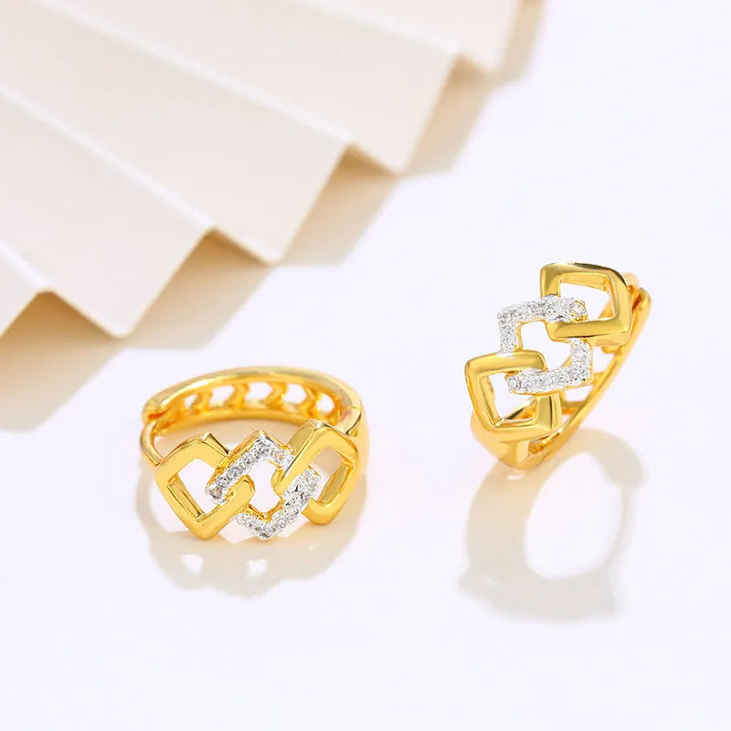 A pair of gold-coloured geometric drop earrings with a hollow out design on a plain background.