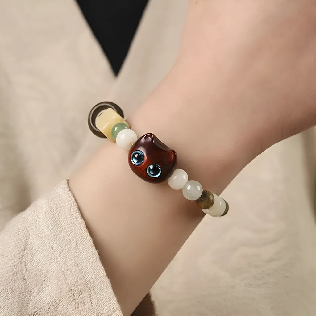 Hand-woven bracelet with jade, bodhi, and guajacwood beads, a multi-treasure cube, and a carved cat's paw charm.