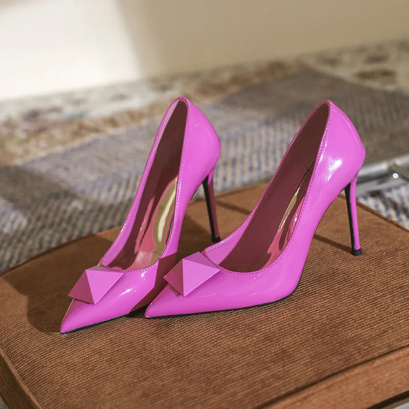Pink patent leather women's stiletto heels with pointed toe and rivet buckle detail.