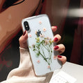 Clear TPU iPhone case with preserved pink dried flowers visible through transparent back cover